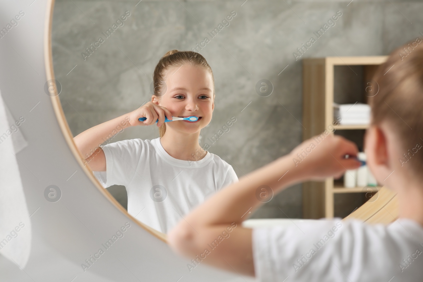 Photo of Cute little girl brushing her teeth with plastic toothbrush near mirror in bathroom