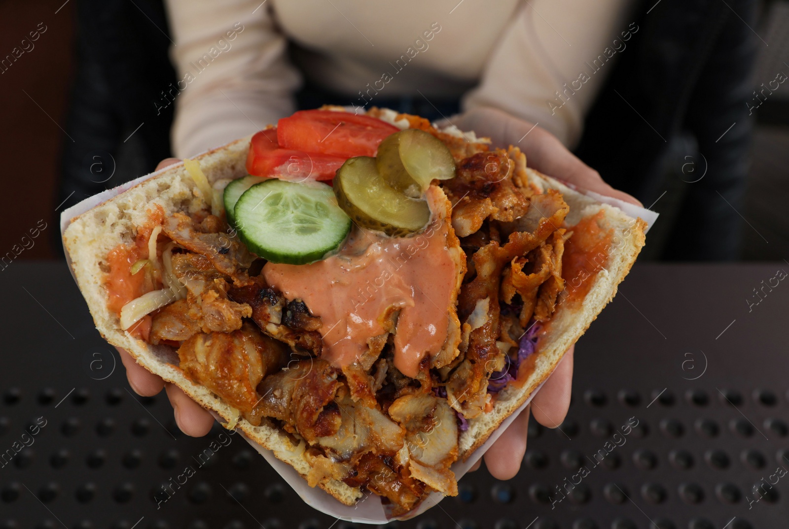 Photo of Woman holding delicious bread with roasted meat and vegetables indoors, closeup. Street food