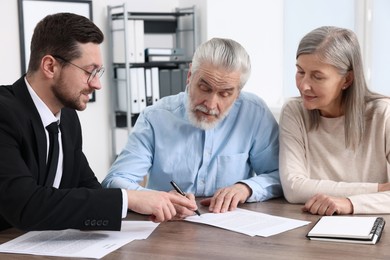 Elderly couple consulting insurance agent about pension plan at wooden table indoors