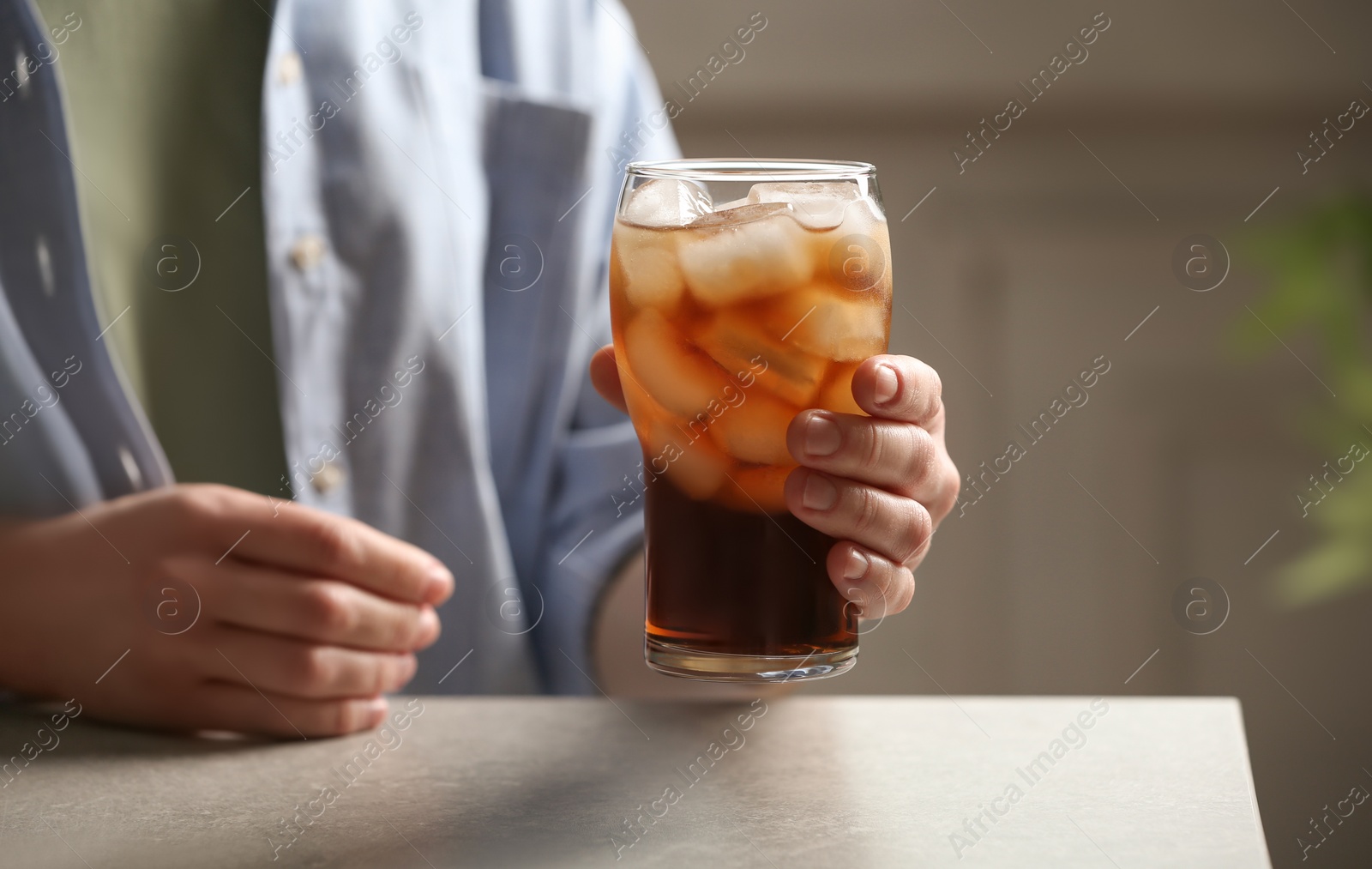 Photo of Woman holding glass of cola with ice at table, closeup. Space for text