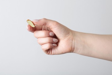 Photo of Woman holding vitamin capsule on light grey background, closeup. Health supplement