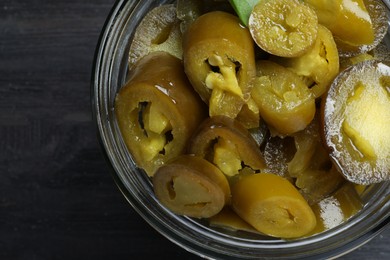 Glass jar with slices of pickled green jalapeno peppers on black wooden table, top view