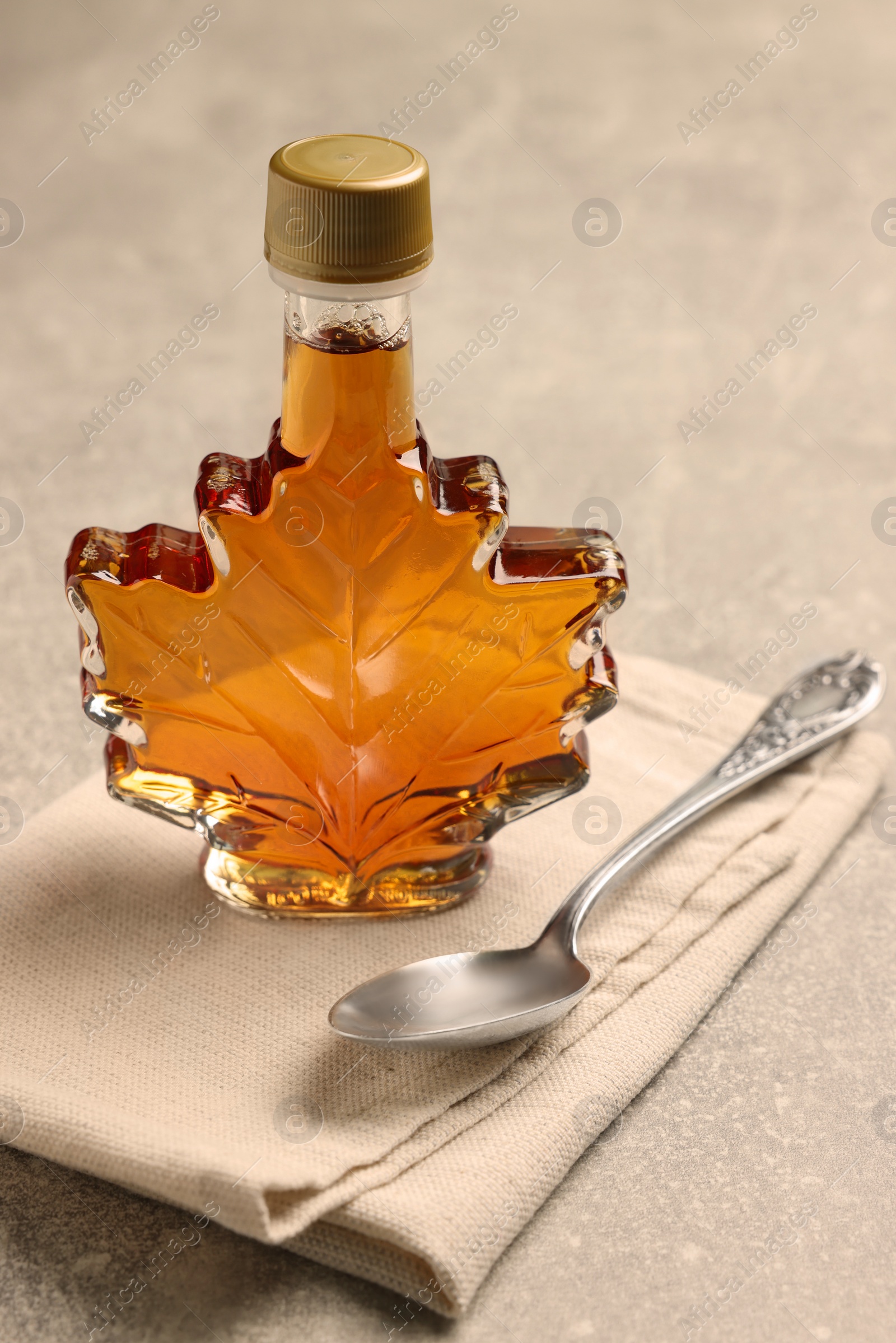 Photo of Leaf shaped bottle of tasty maple syrup and spoon on light grey table