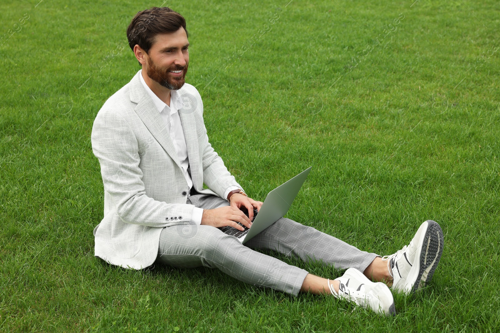 Photo of Handsome businessman with laptop on green grass outdoors