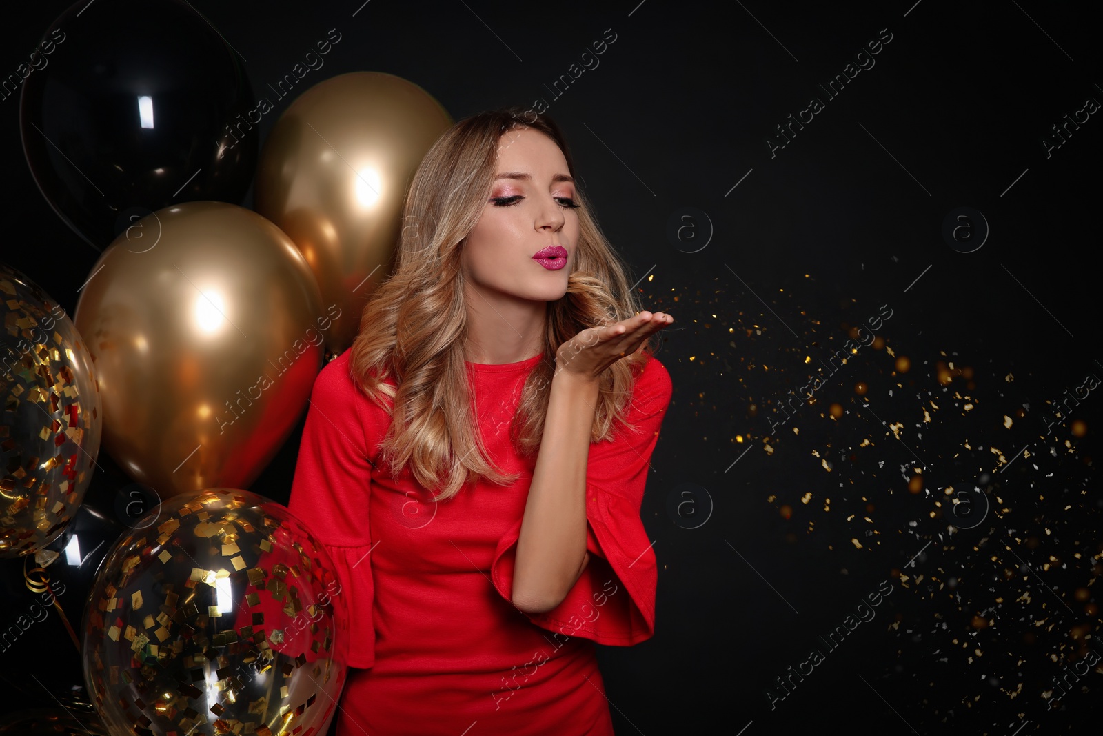 Photo of Happy woman with air balloons blowing glitter on black background, space for text. Christmas party