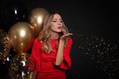 Photo of Happy woman with air balloons blowing glitter on black background, space for text. Christmas party