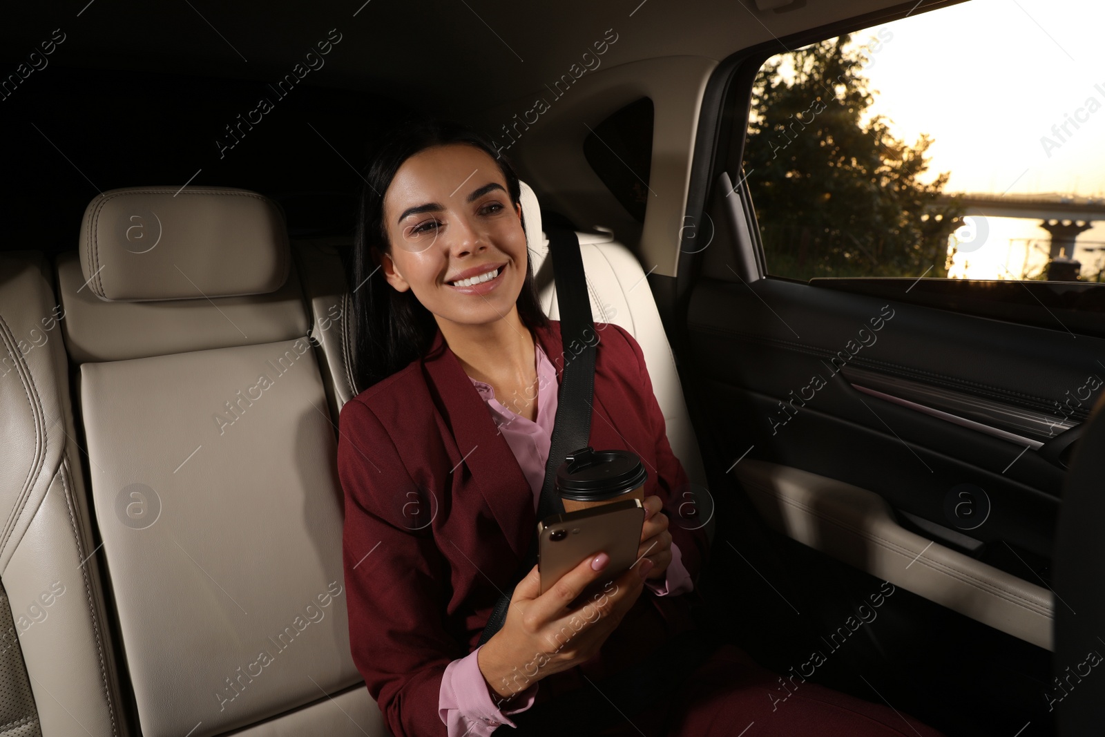 Photo of Young woman with smartphone and cup of drink in modern taxi