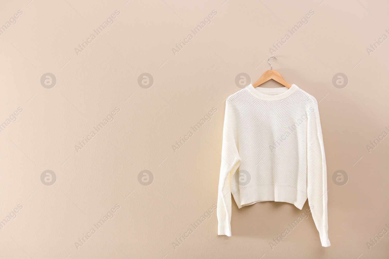 Photo of Hanger with stylish sweater on beige wall. Space for text