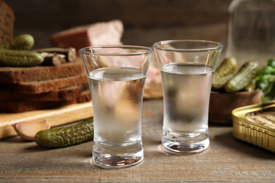 Photo of Cold Russian vodka with snacks on wooden table, closeup