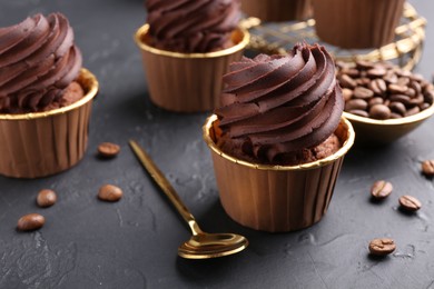Photo of Delicious chocolate cupcakes and coffee beans on black textured table, closeup
