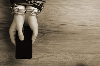 Top view of internet addicted woman with chained hands using smartphone at wooden table, space for text. Sepia effect