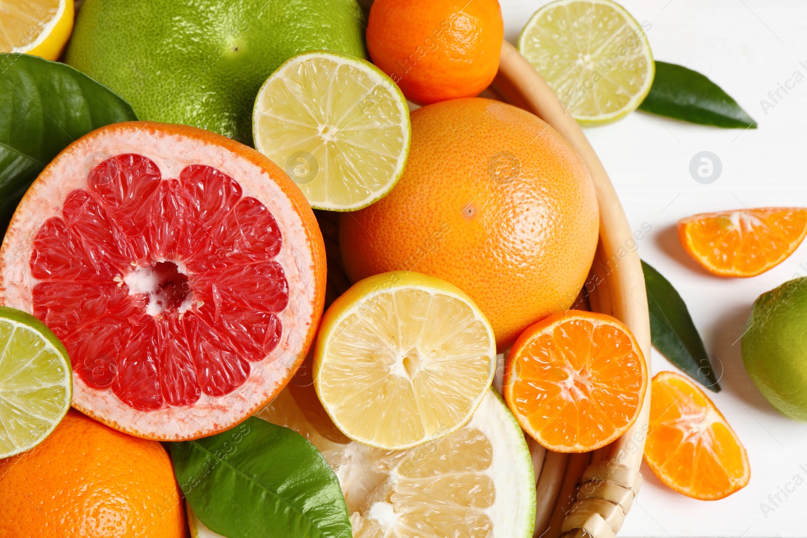 Photo of Different ripe citrus fruits with green leaves on white wooden table, flat lay