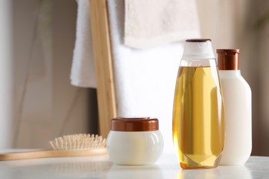 Photo of Shampoo, conditioner and hair mask near brush on white table in bathroom, space for text
