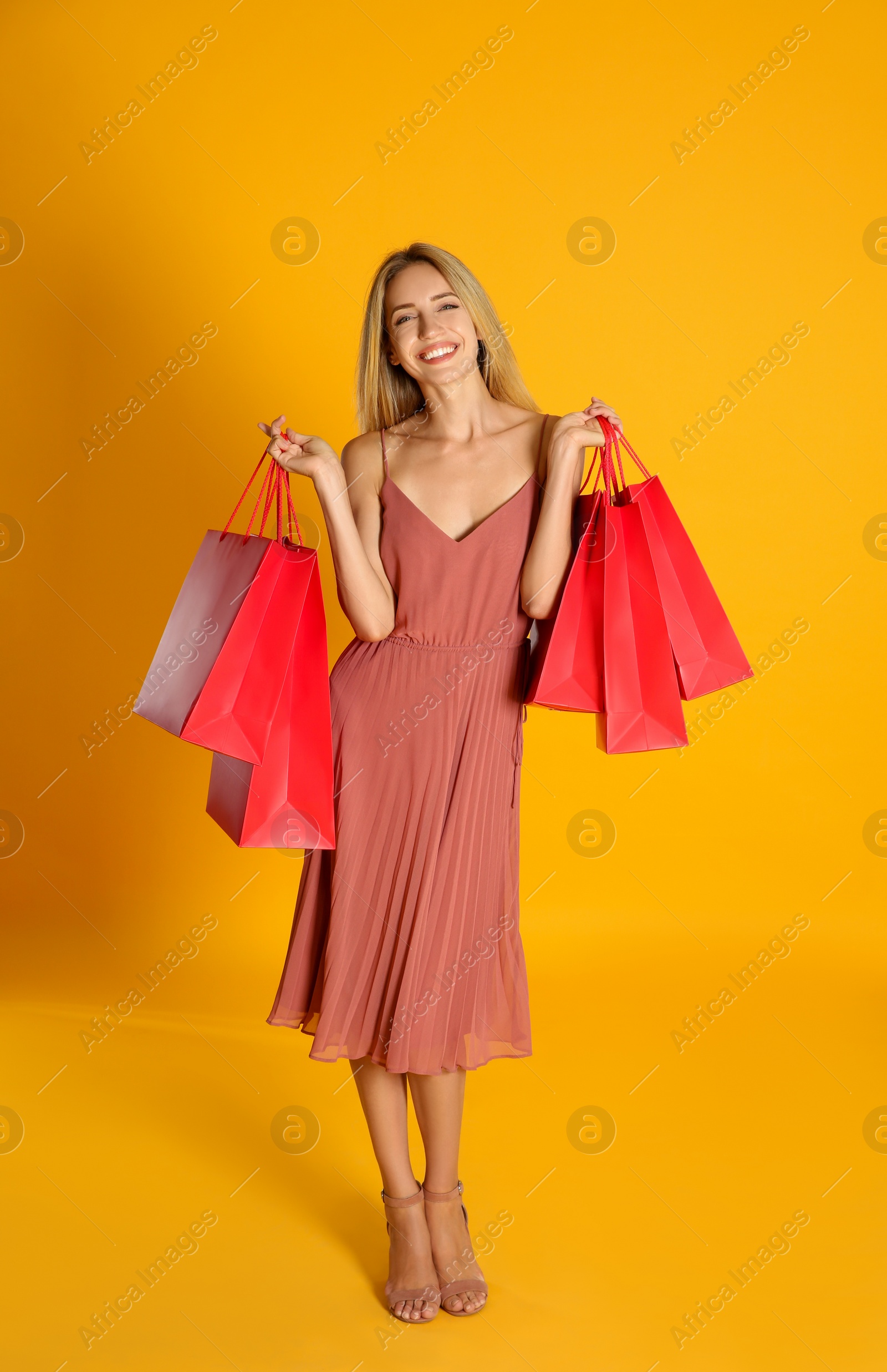 Photo of Happy young woman with shopping bags on yellow background. Black Friday Sale