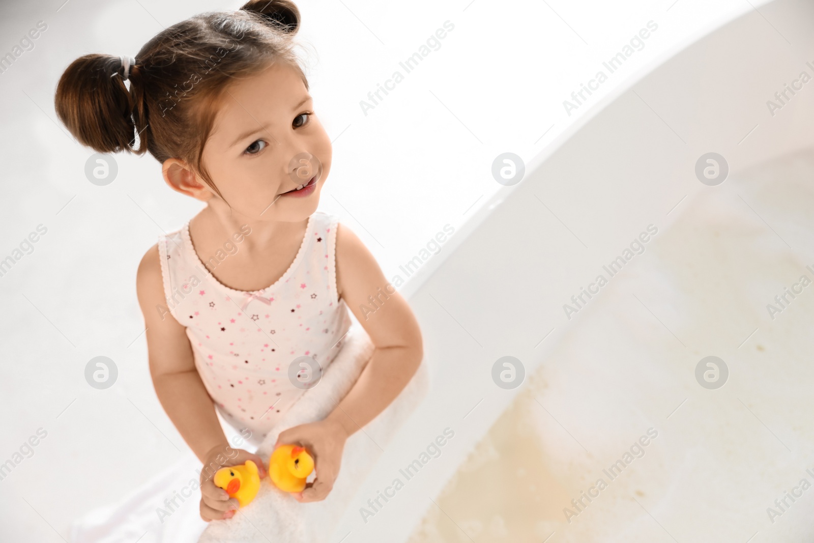 Photo of Cute little girl near tub in bathroom. Space for text