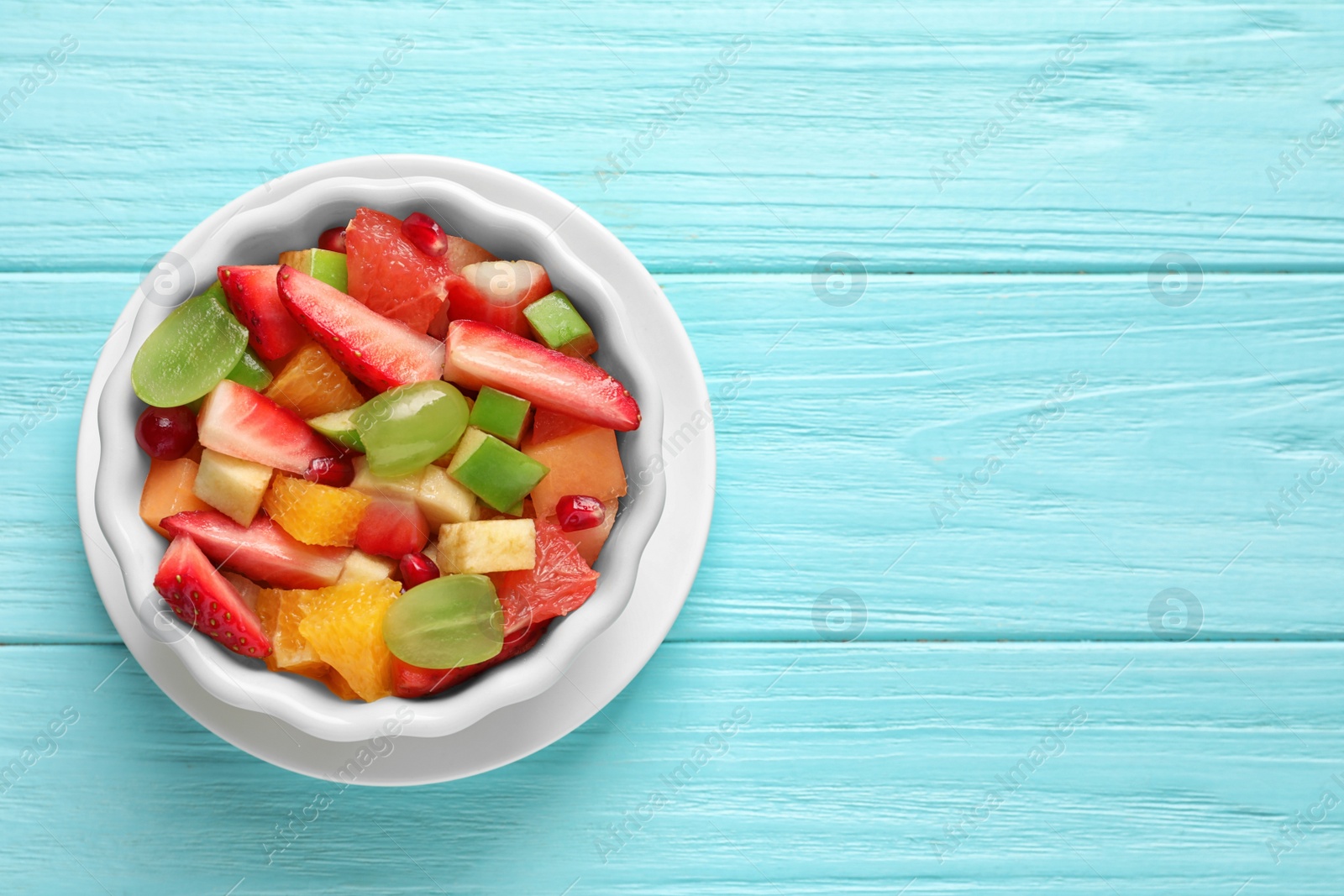 Photo of Bowl with fresh cut fruits on wooden table, top view