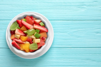 Bowl with fresh cut fruits on wooden table, top view