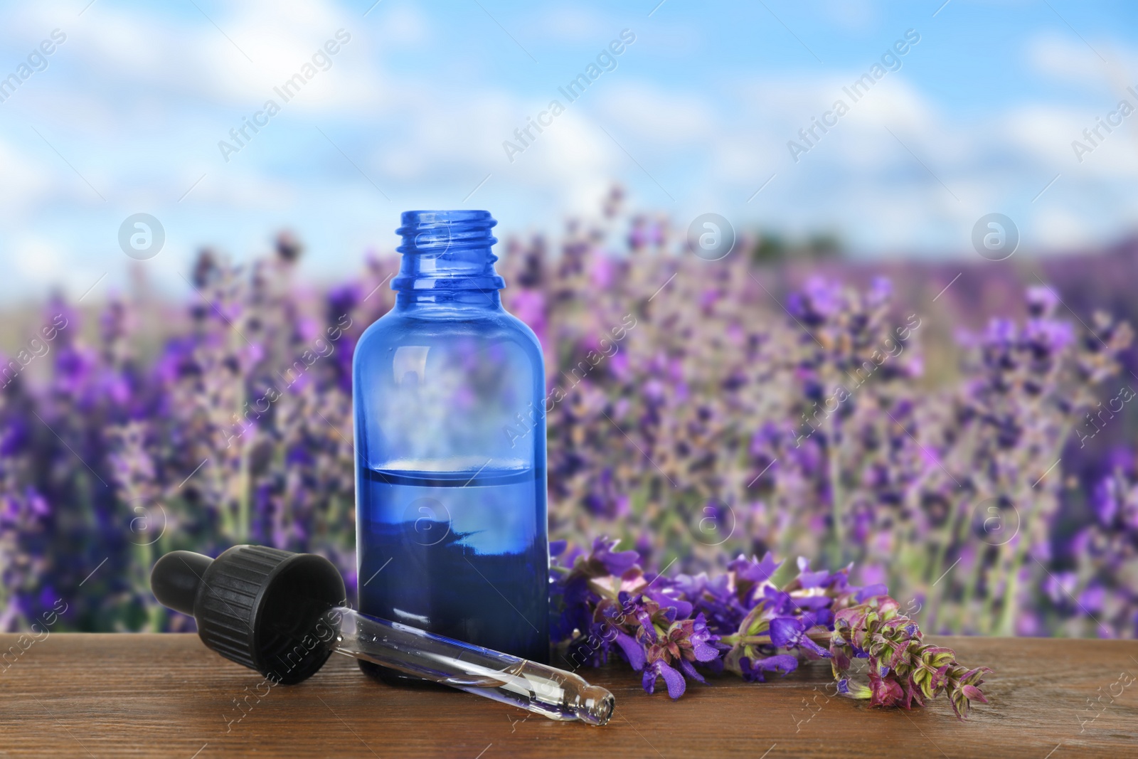 Image of Bottle of essential oil and sage flowers on wooden table against blurred background