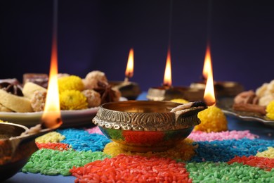 Diwali celebration. Diya lamps and colorful rangoli on table against violet background, closeup