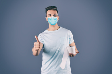 Image of Man in medical mask holding toilet paper roll on grey background