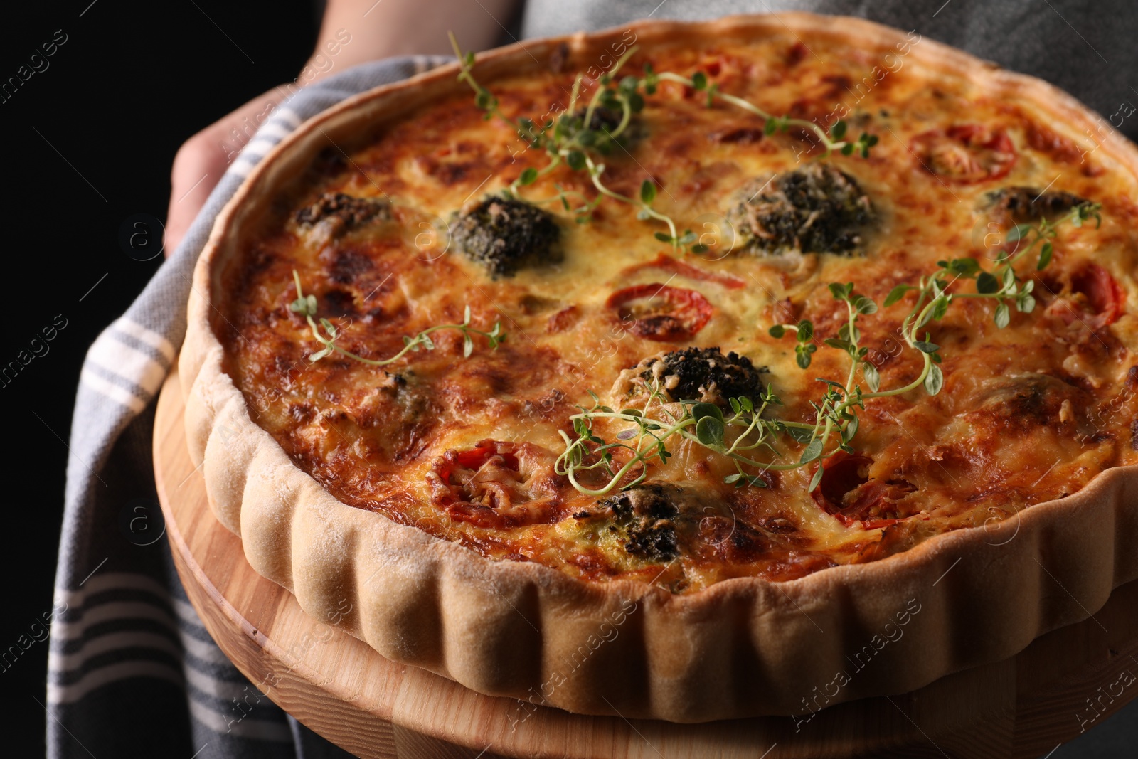 Photo of Woman holding delicious homemade vegetable quiche on black background, closeup