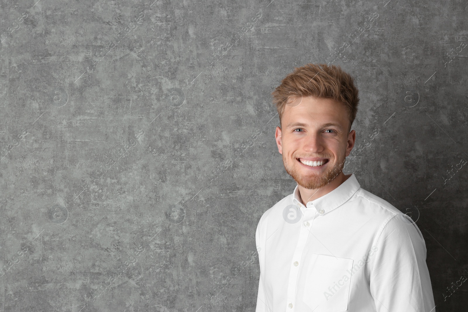 Photo of Portrait of handsome young man near grey wall. Space for text