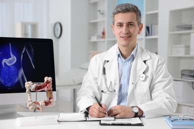 Photo of Gastroenterologist with anatomical model of large intestine working at table in clinic