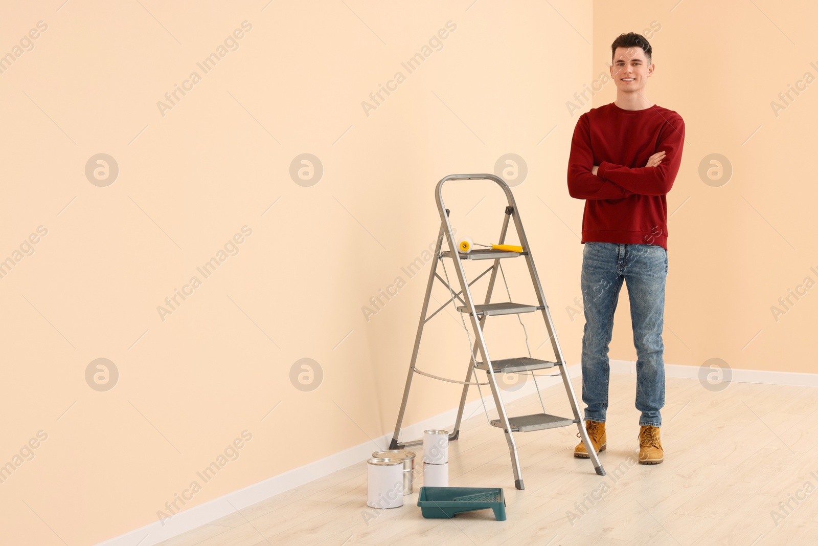 Photo of Young handsome man near metal stepladder and painting tools indoors, space for text. Room renovation