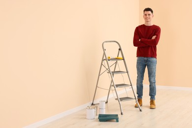 Young handsome man near metal stepladder and painting tools indoors, space for text. Room renovation