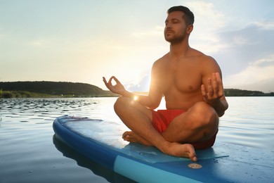 Photo of Man meditating on light blue SUP board on river at sunset