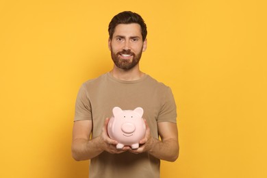 Photo of Happy man with ceramic piggy bank on orange background