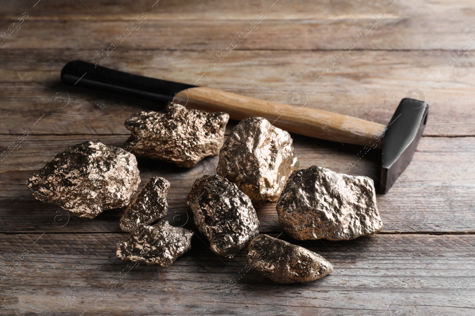 Photo of Pile of gold nuggets and hammer on wooden table