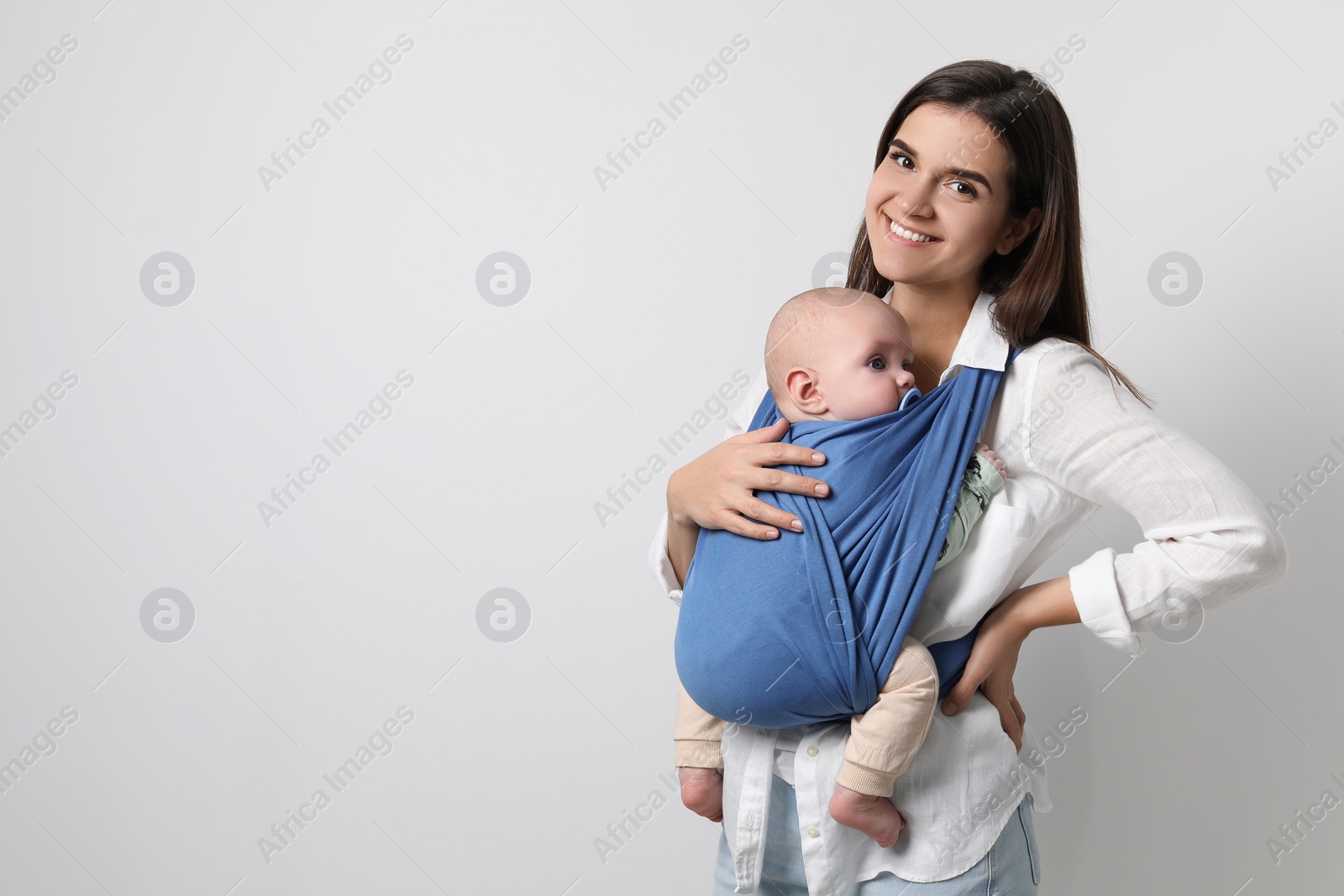 Photo of Mother holding her child in sling (baby carrier) on light grey background. Space for text