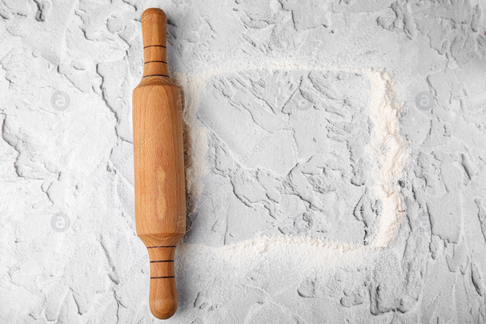 Photo of Frame made of flour and rolling pin on white textured table, top view. Space for text