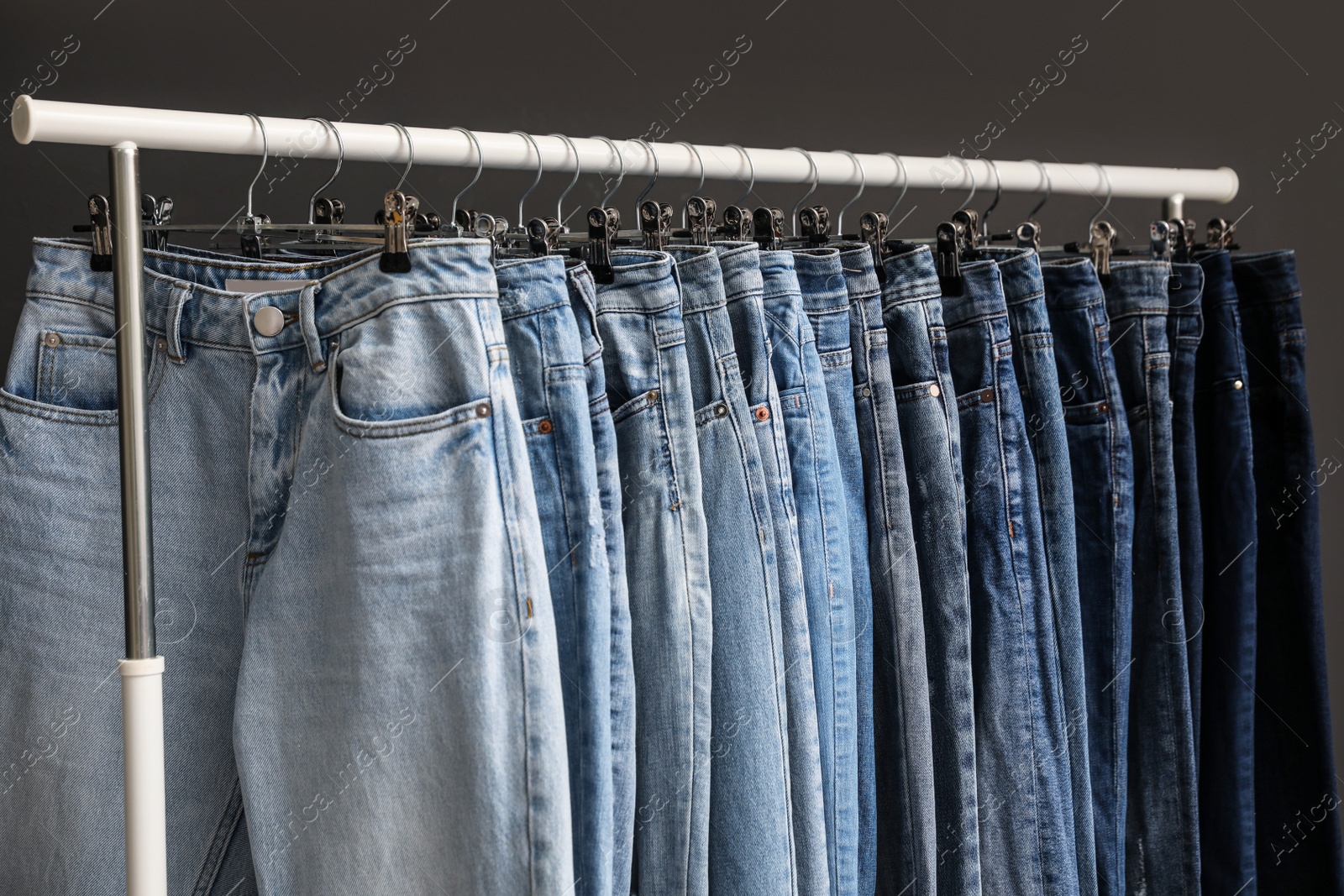 Photo of Rack with different jeans on dark grey background, closeup