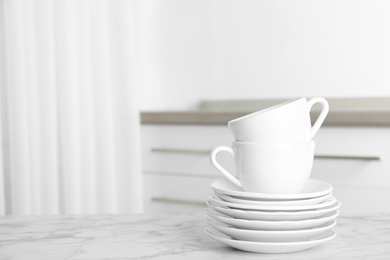 Photo of Stack of clean plates and cups on marble table in kitchen. Space for text