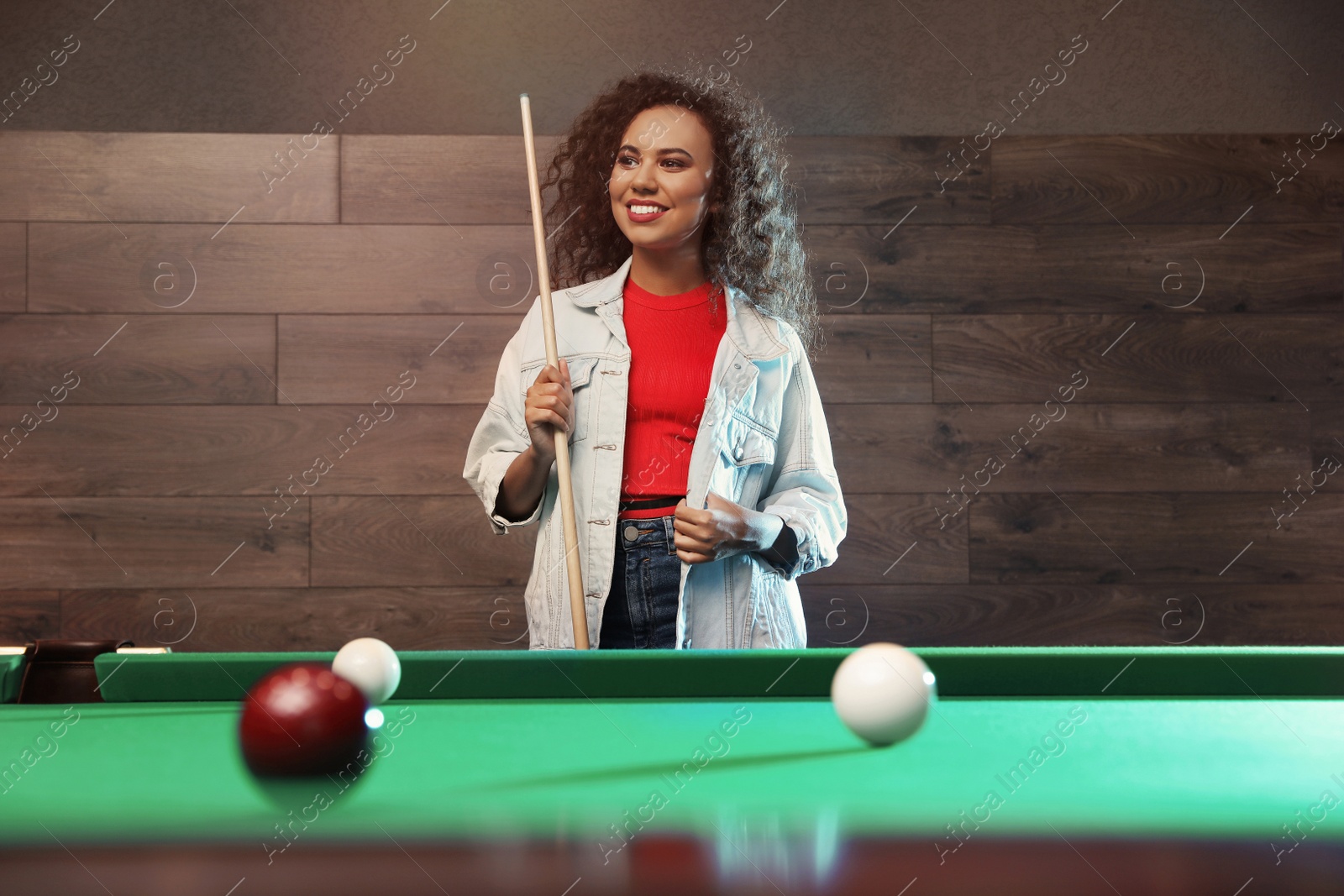 Photo of Young African-American woman with cue near billiard table indoors