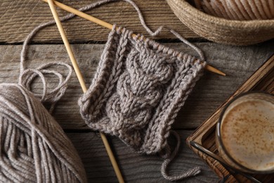Photo of Soft grey woolen yarn, knitting, needles and glass of coffee on wooden table, flat lay