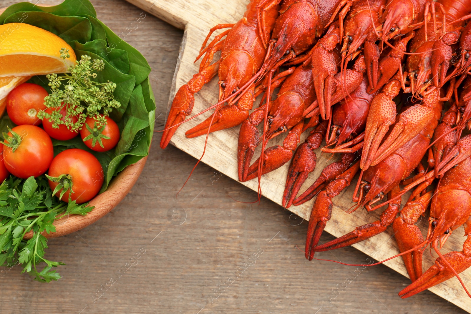 Photo of Delicious red boiled crayfish and products in bowl on wooden table, top view