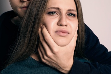 Man abusing young woman on light background. Stop sexual assault