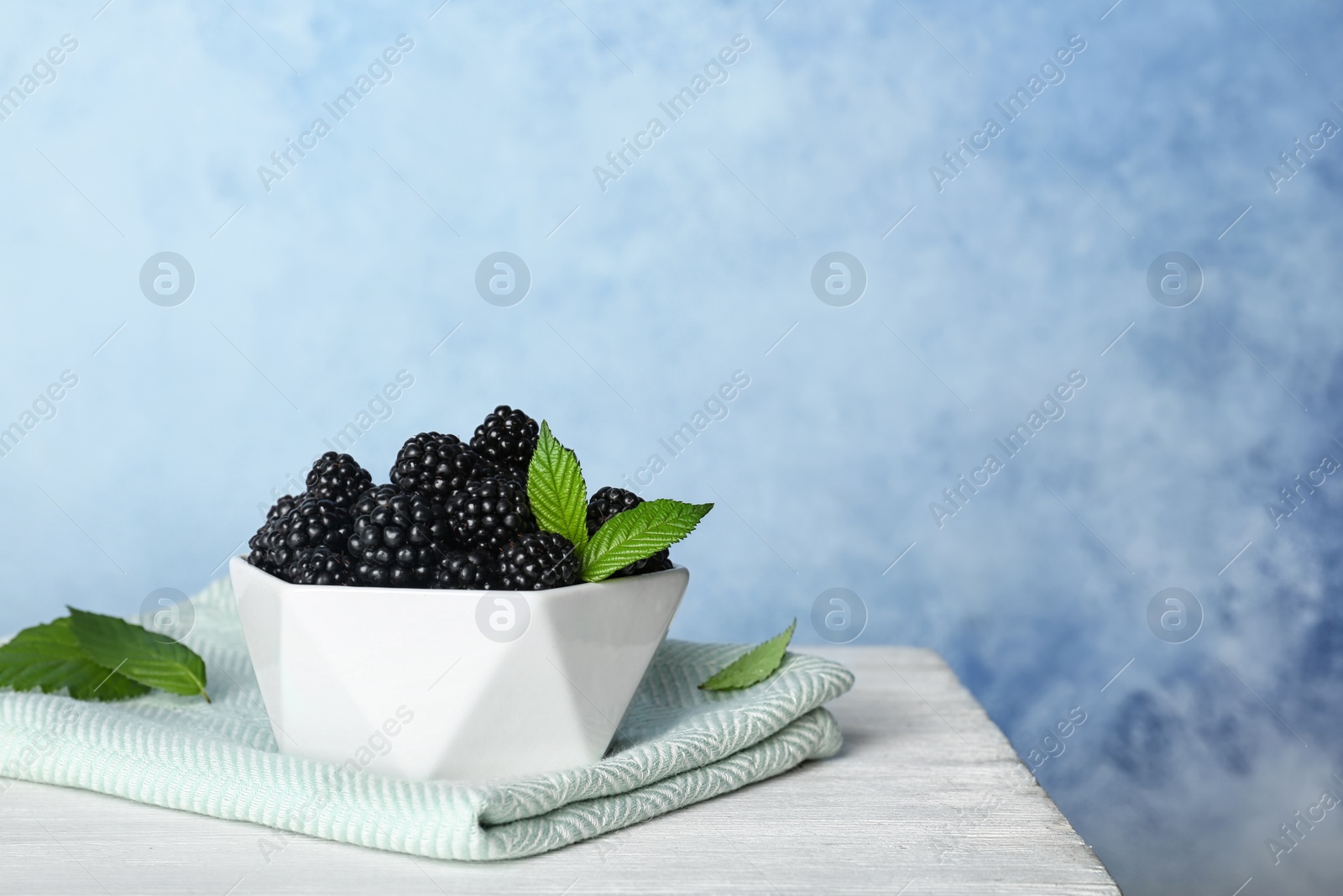 Photo of Bowl of fresh blackberry on table against color wall. Space for text