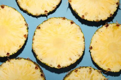 Photo of Slices of tasty ripe pineapple on light blue background, flat lay