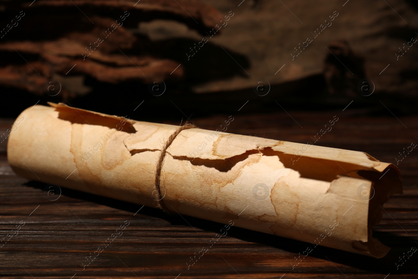 Photo of Scroll of old parchment paper on wooden table, closeup