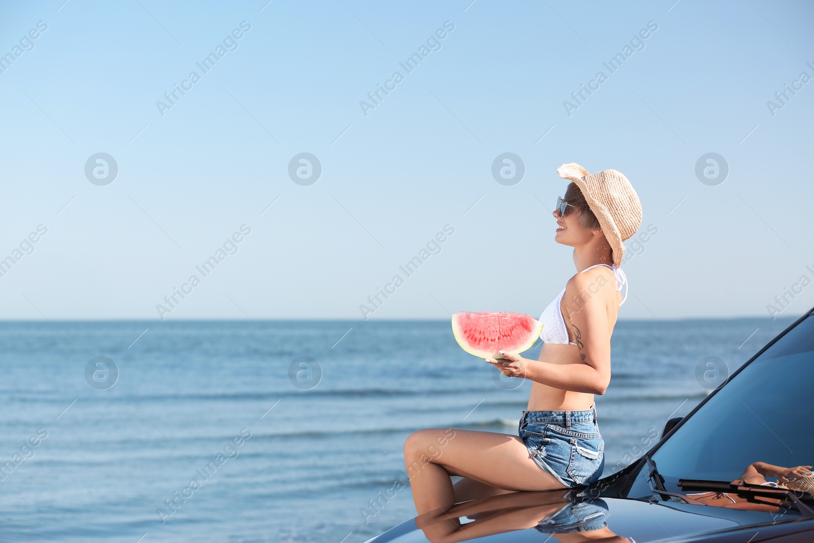 Photo of Young woman with watermelon slice near car on beach. Space for text