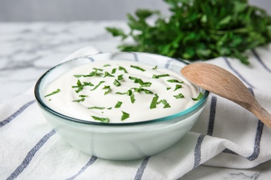 Glass bowl of fresh sour cream with parsley and wooden spoon on marble table