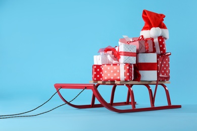 Photo of Sleigh with gift boxes and Santa hat on light blue background. Space for text