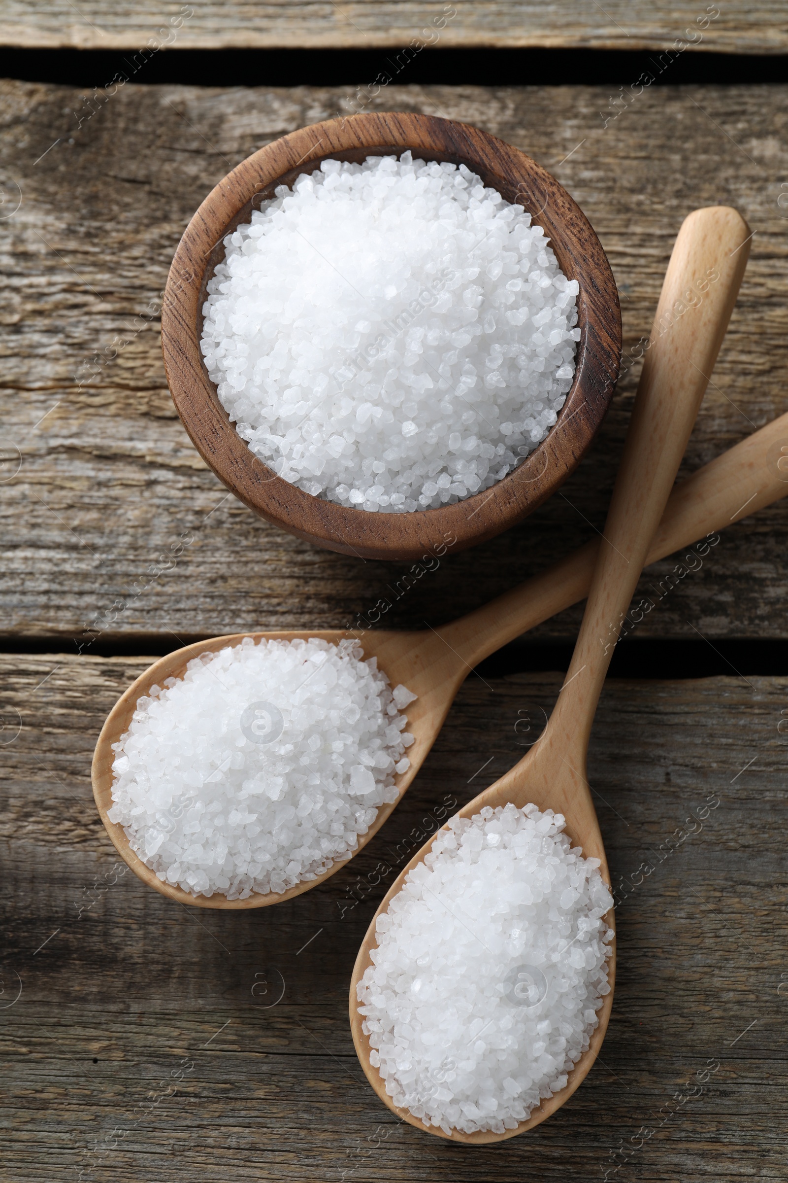 Photo of Organic salt in bowl and spoons on wooden table, flat lay