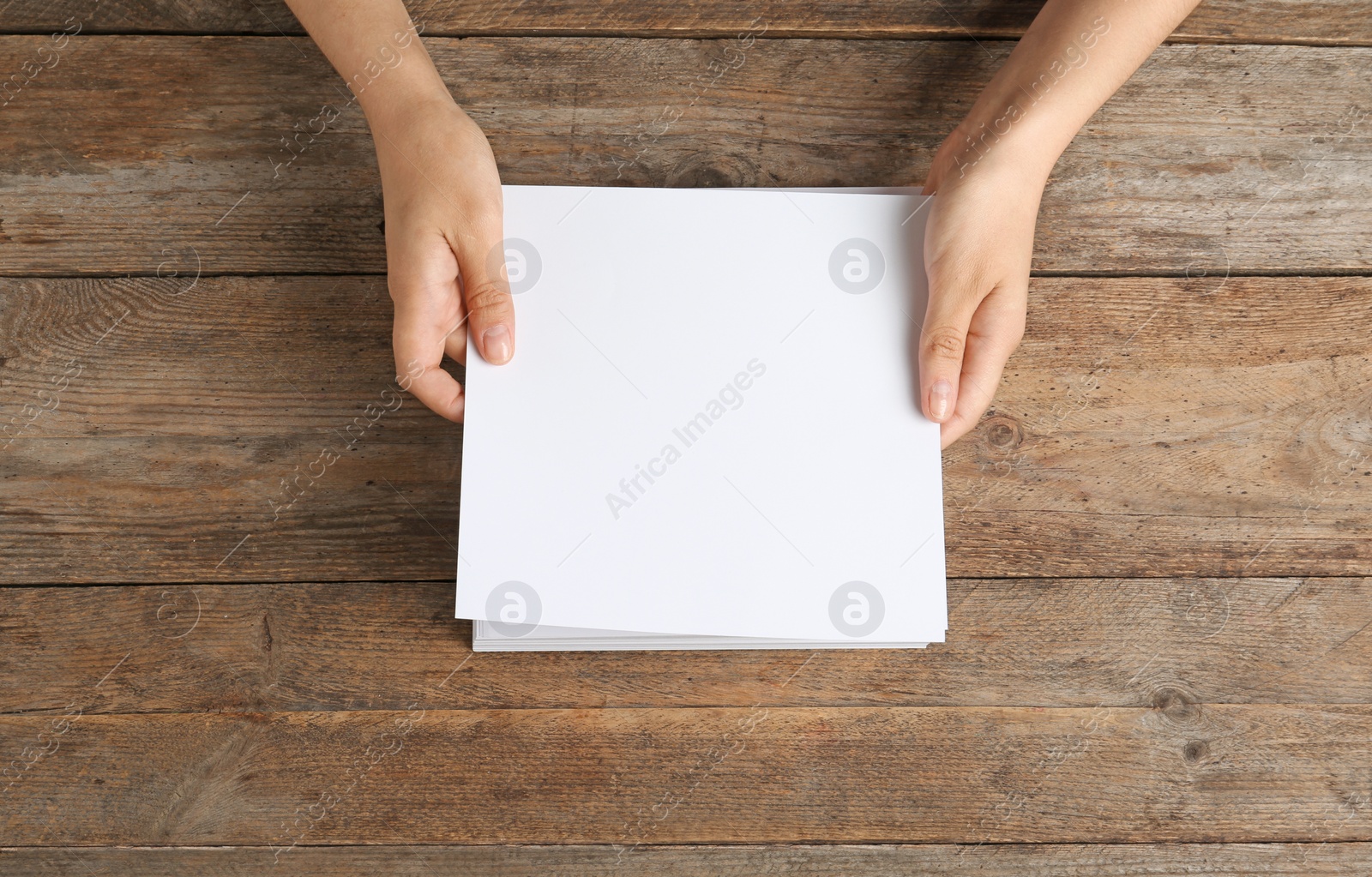 Photo of Woman holding blank paper sheets for brochure at wooden table, top view. Mock up