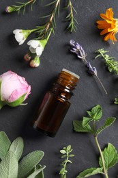 Bottle of essential oil, different herbs and flowers on black table, flat lay