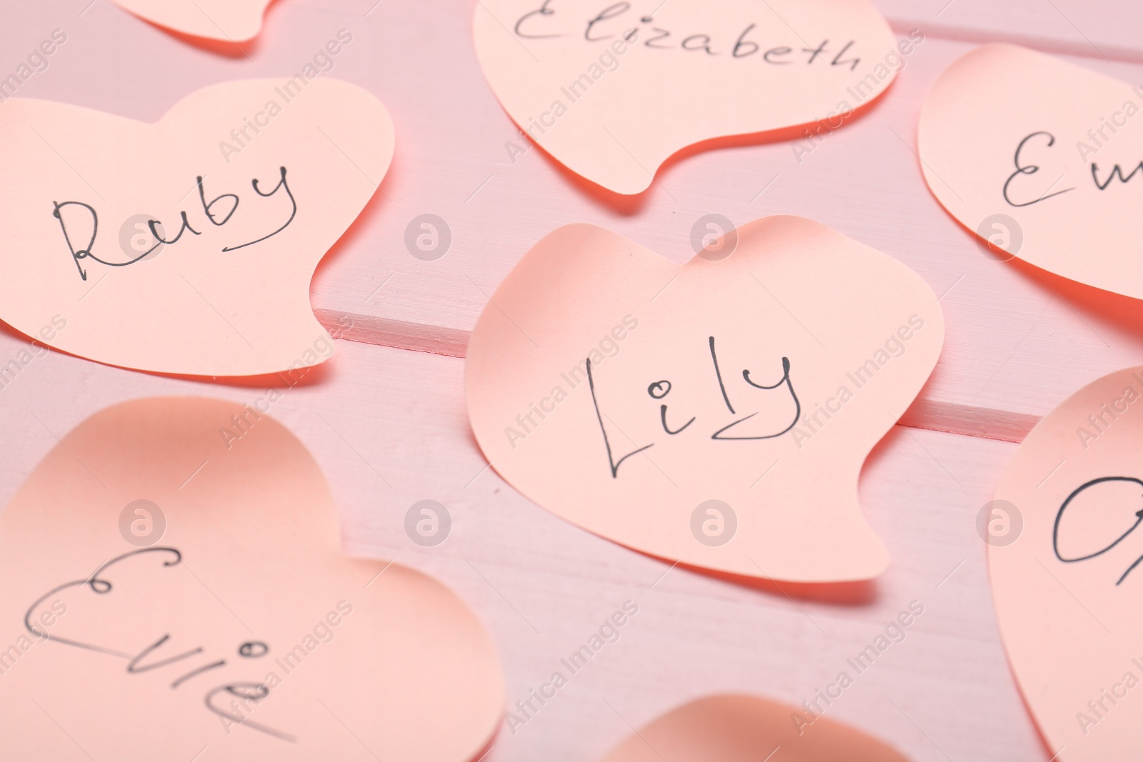 Photo of Paper stickers with different names on pink wooden table, closeup. Choosing baby's name